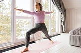 woman doing “warrior” yoga pose in her living room