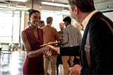 A woman in a red dress holding a clipboard and shaking a mans hand