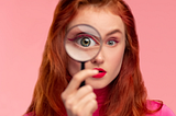 Red headed woman looks through a magnifying glass.