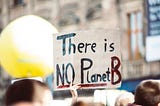 A hand holds up a sign that says THere is NO Planet B