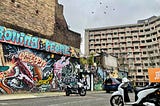 Cityscape. Brick wall covered in graffiti next to an apartment block with some birds in the sky.