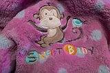 A pink and white polka-dotted blanket with an embroidered monkey and “Sweet baby”