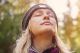 Young blonde woman with eyes closed in outdoor environment