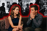 An image of an attractive man and woman sitting on a couch talking. The woman looks hesitant, and the man looks mortified as he assumes he has been rejected.