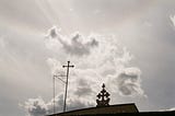 A cloudy sky with two crosses on top of a church roof.
