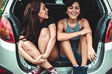 Image of two females laughing in the back of a Subaru