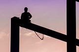 Silhouette of a construction worker sitting  on a high girder against a pink sky.