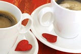 Two cups and saucers with coffee and a red hear on each saucer