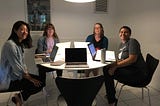 Four writers together at a circular table with their laptops open. They are the Foothill Poets, 2018