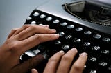 Hands touch the letter keys on a typewriter.