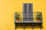 A wrought iron balcony against a yellow wall