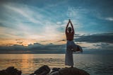 Person doing yoga tree pose by the water