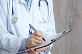 A doctor wearing a white lab coat and stethoscope holds a clipboard and pen.