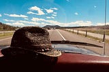 Straw hat resting on the dashboard of a car rolling on a road, sunny day blue skies.