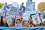 Image of people holding signs saying things like “Science” and “Science Serving the Common Good”