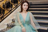 A picture of Abby Choi dressed in a gorgeous blue dress seating on stairs.