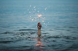 A hand in the sea holding up a sparkler