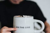 A child pointing to a coffee mug with the phrase “See the Good” written on it.