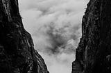 Black and white image of a mountain pass with a runner in between two rock faces and lots of white cloud