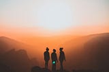 A silhouette of three women standing on a mountain.