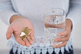 Woman holding a glass of water in her left hand and multiple pills in her right.