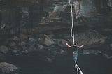A man walking across a tightrope hanging over a chasm