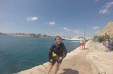 Emily on the dock of a bay in Malta, decked out in all her scuba diving gear with a big smile on her face