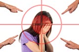 A woman covering her face with her hands in shame while fingers point frim wvery direction.