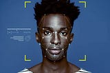 A dark-skinned person stares directly at the screen with facial recognition mapping points symmetrically placed around their face.