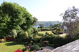 Photograph of trees and sweeping lawns with a view of the Helford river in the distance.