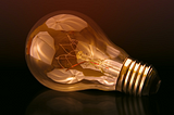 A lightbulb lying on its side, with white umbrellas reflected in the glass.