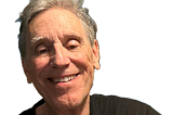 Smiling older man with gray hair wearing a black shirt, shown against a transparent background.