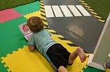 Young child laying on their stomach in the middle of a play area, typing away at a fake laptop.