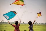 Two little boys flying kites in a field in India