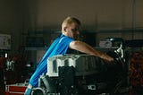 A side profile of an auto mechanic student working on an engine