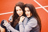 two girls with brown hair sitting on orange painted floor hugging