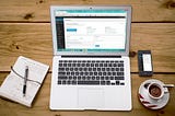 Laptop showing Wordpress Admin dashboard, with coffee and notbook sitting on a table.