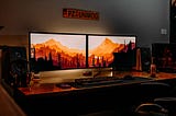 A computer desk with two monitors displaying a mountain photograph on sunset.