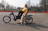 An old woman on an accessible tricycle with a guide dog beside her