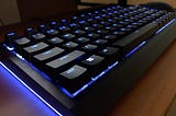 A Razer Blackwidow V4 75 keyboard on a desk, with the lighting set to a blue hue.