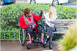 Person in wheelchair high-fiving person on park bench. From Getty Images.