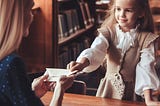 Image of a young girl handing a folded note to a lady in the library