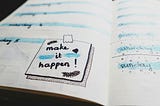 A photo of a planning notebook with  message 'make it happen' written on a page