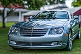 Panoramic photograph of a (likely) 2013 Chrysler Crossfire with a red polebarn in the background.