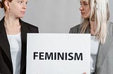 Two white women holding a feminism sign.