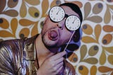 Man sticking his tongue out while holding a clock like sunglasses