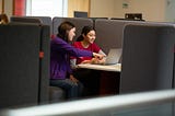 Two students sitting in a booth looking at a laptop screen