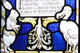 A stained glass window of the White Rabbit and the Dodo, commemorating Lewis Carroll, author of Alice in Wonderland. The White Rabbit is, as ever, anxiously checking his pocket watch.