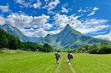 Image of Author’s husband and friends walking the Juliana Trail in a green meadow with alps in the background.