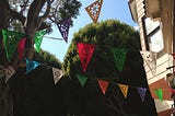 Multi-colored streamer flags in a tree-lined neighborhood with blue skies